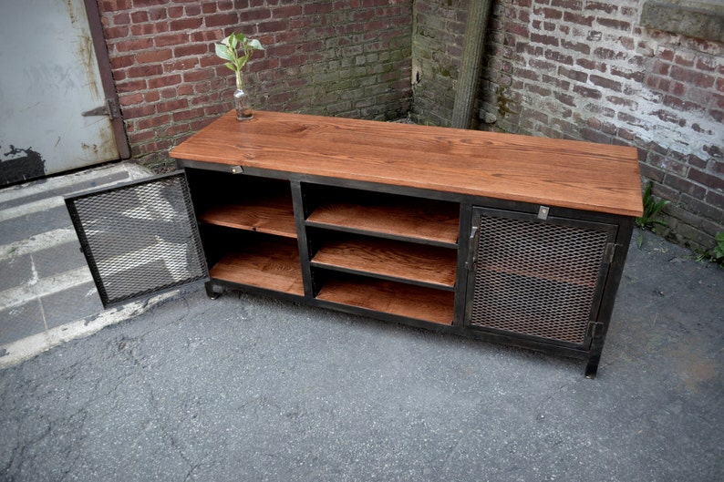 May include: A rustic, industrial-style cabinet with a reddish-brown wooden top and shelves. The cabinet has a black metal frame and a door with a mesh design. The cabinet is designed for storage.