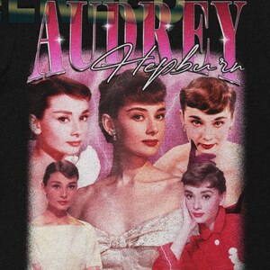 May include: Black t-shirt featuring a collage of Audrey Hepburn images with the text "Audrey Hepburn" in a pink and purple retro font. The shirt has a vintage, distressed aesthetic, perfect for fans of classic Hollywood.