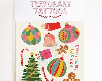May include: A sheet of temporary Christmas-themed tattoos featuring a Christmas tree, ornaments, candy canes, a gingerbread man, a gift box, and a mitten. The text "CHE12FW12 WEKKA" is printed on the sheet.