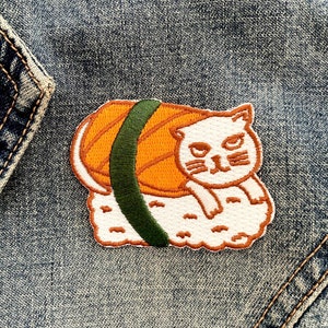 May include: A white cat with orange and green sushi on a denim background. The cat is lying on its side with its head resting on the sushi.