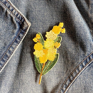May include: A yellow embroidered flower patch with green leaves, ideal for adding a touch of nature to denim jackets, bags, or other fabric items.