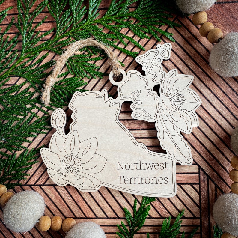 May include: A wooden ornament shaped like the Northwest Territories of Canada with a floral design and the text "Northwest Territories".