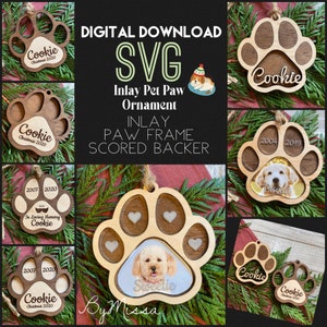 May include: Digital download SVG file for a pet paw ornament. The ornament is made of wood and has a cutout in the shape of a paw print. The paw print has a space for a photo of a pet. The ornament is also scored for easy assembly. The text "Inlay Pet Paw Ornament" and "Inlay Paw Frame Scored Backer" is visible in the image.
