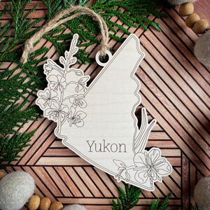 May include: Wooden ornament shaped like the Yukon Territory with a floral design and the word "Yukon" inscribed on it.