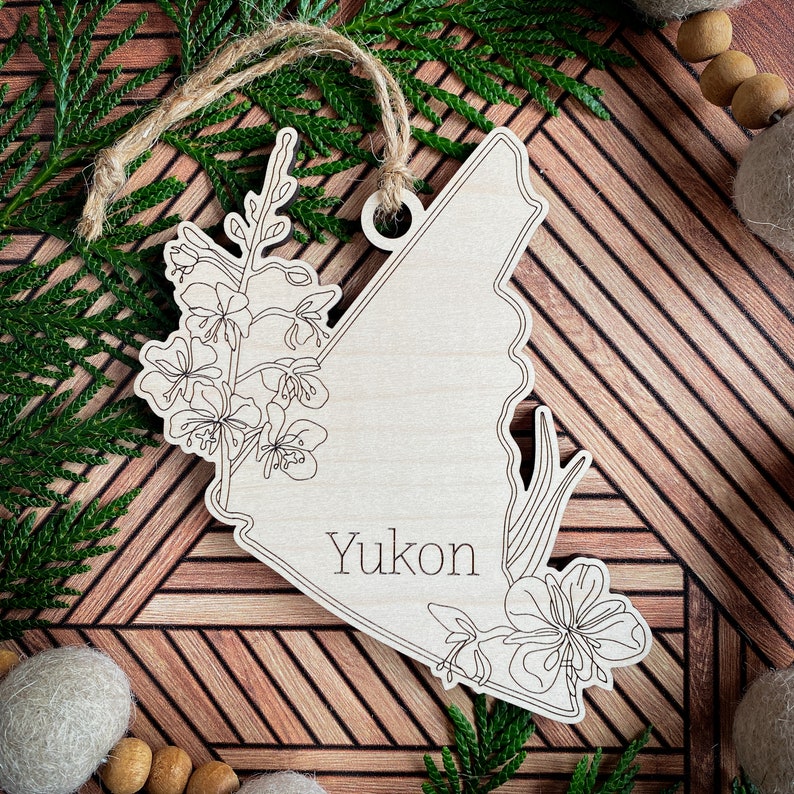 May include: Wooden ornament shaped like the Yukon Territory with a floral design and the word "Yukon" inscribed on it.