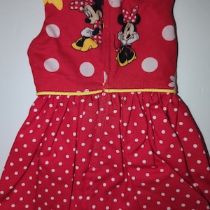 Puede incluir: Vestido rojo con lunares blancos y dibujos de Minnie Mouse. El vestido sin mangas tiene un ribete amarillo y una cremallera en la espalda. El vestido est&aacute; hecho de una tela suave.