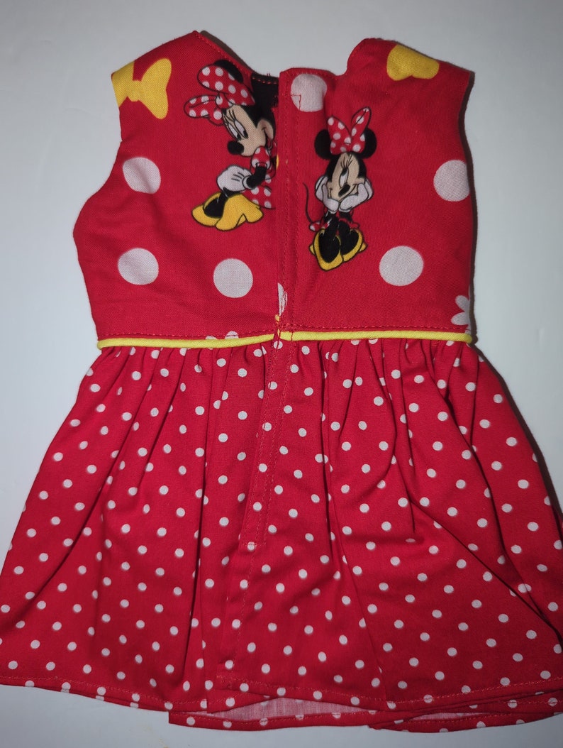 Puede incluir: Vestido rojo con lunares blancos y dibujos de Minnie Mouse. El vestido sin mangas tiene un ribete amarillo y una cremallera en la espalda. El vestido est&aacute; hecho de una tela suave.