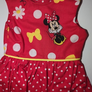 Puede incluir: Vestido rojo sin mangas con lunares blancos y ribete amarillo. El vestido presenta una imagen de Minnie Mouse, margaritas blancas y lazos amarillos. La falda est&aacute; fruncida y el vestido es de tela ligera.