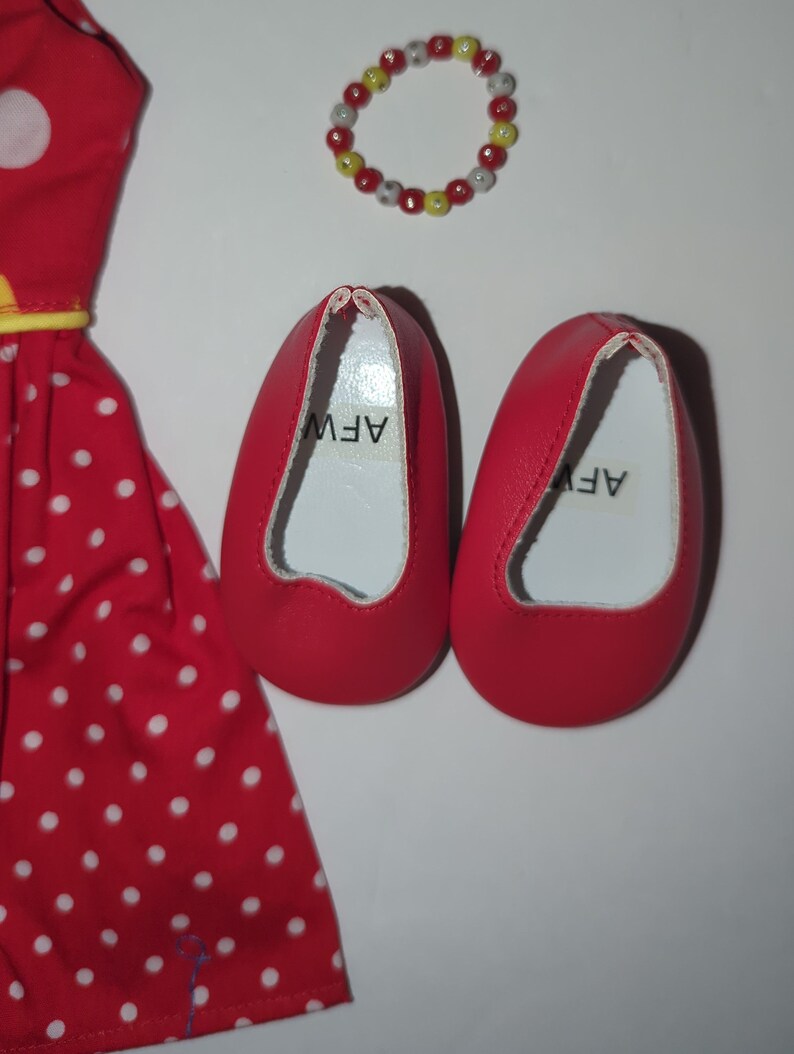 Puede incluir: Un vestido rojo con lunares blancos, zapatos rojos y una pulsera de cuentas. El vestido tiene lunares blancos y un ribete amarillo. Los zapatos rojos tienen las letras "AFW" impresas en el interior. La pulsera tiene cuentas rojas, amarillas y blancas.