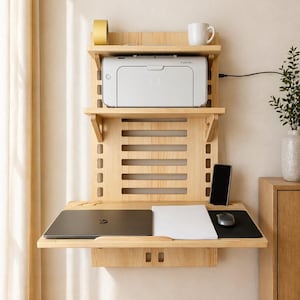 Könnte beinhalten: Ein helles, an der Wand montiertes Holzschreibtisch mit mehreren Regalen. Das obere Regal enthält einen Drucker und eine Tasse. Der mittlere Abschnitt hat ein geschlitztes Design. Das untere Regal hat einen Laptop, Papier, eine Maus und ein Smartphone.