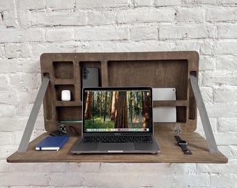 May include: A dark brown wooden wall-mounted desk with a laptop, phone, and other accessories. The desk folds down for space-saving storage.