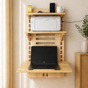 May include: A wall-mounted wooden desk with three shelves. The top shelf holds a yellow tape roll, a mouse, a smartphone, and a white mug. The middle shelf has a white printer. A laptop sits on the desk shelf below.