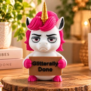 May include: A white unicorn figurine with a bright pink mane and a gold horn. The unicorn has a grumpy facial expression and holds a brown rectangular sign that features the black text "Glitterally Done" in a bold, sans-serif font.