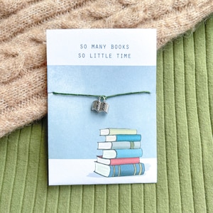May include: A green string bracelet with a silver book charm. The bracelet comes with a card that reads "So many books, so little time" and features an illustration of a stack of books.