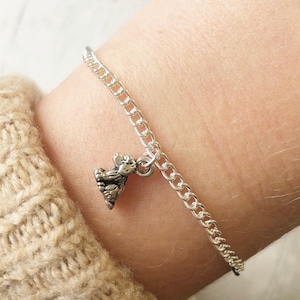 May include: A silver chain bracelet with a small silver bear charm. The bracelet is on a person's wrist.