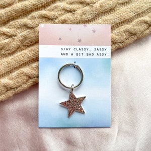 May include: A silver star-shaped keyring with a ring attached. The keyring is on a card with the text "Stay Classy, Sassy and a Bit Bad Assy".