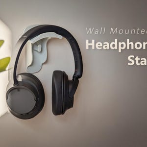 Peut inclure: Un support mural blanc pour casque audio avec un casque noir suspendu. Le support est intitulé "Support mural pour casque audio".