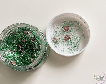 May include: A clear glass jar filled with green glitter and small football-shaped embellishments. Next to it, a white lid contains similar glitter and football accents. The jar is open, revealing the contents.