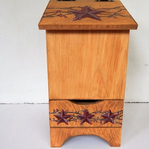 May include: A wooden storage box with a drawer. The box is painted a light brown color and has a decorative design of red stars and berries on the top and bottom.