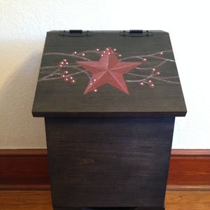 May include: A dark brown wooden storage box with a hinged lid. The lid is decorated with a red star and a painted design of branches with red berries. The box has a drawer with a similar design on the front.