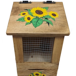 May include: A wooden storage bin with a wire mesh front and a drawer. The top of the bin has a painted design of sunflowers with green leaves. The bin has black metal hinges on the top.