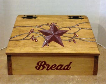 May include: Wooden bread box with a red star and berry design on the lid. The box is painted brown and has the word "Bread" written on the front.
