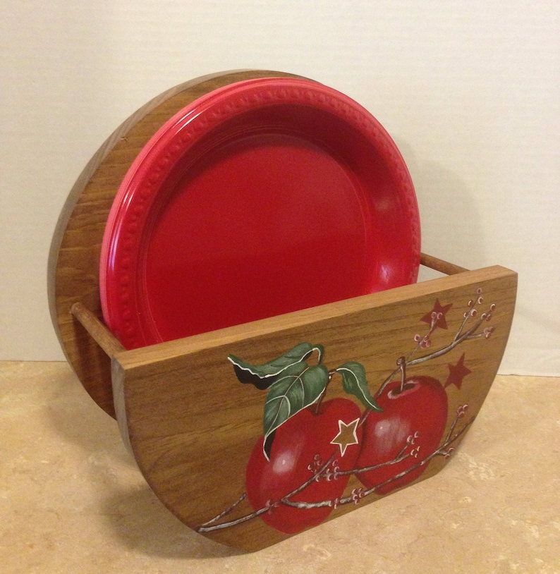 May include: Wooden plate holder with a hand-painted design of red apples and green leaves. The holder is made of brown wood and has a rustic look.