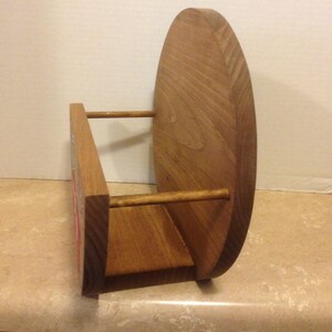 May include: A wooden wall-mounted shelf with a rounded back and two horizontal wooden dowels. The shelf is stained a light brown color.
