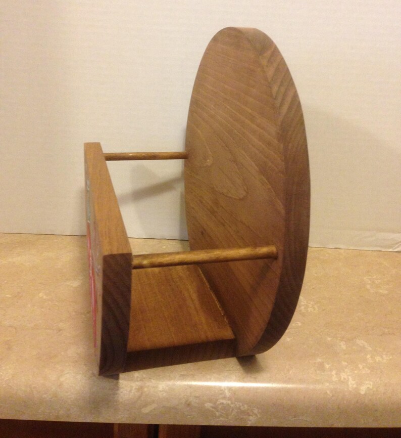 May include: A wooden wall-mounted shelf with a rounded back and two horizontal wooden dowels. The shelf is stained a light brown color.