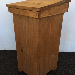 May include: A wooden trash can with a hinged lid. The lid has a metal hinge and the word "Trash" is engraved on the top.