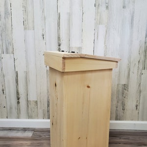 May include: A natural wood bin with a hinged lid. The bin is made of unfinished pine wood and has a simple, rustic design.