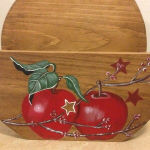 May include: A wooden wall-mounted mail holder with a half-circle top and a painted design of two red apples with green leaves and white stars on a branch with small pink flowers.