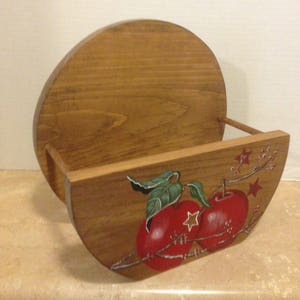 May include: A wooden wall-mounted shelf with a rounded front and a painted design of two red apples with green leaves and white stars on a branch. The shelf is made of natural wood and has a rustic look.