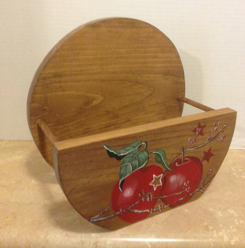 May include: A wooden wall-mounted shelf with a rounded front and a painted design of two red apples with green leaves and white stars on a branch. The shelf is made of natural wood and has a rustic look.