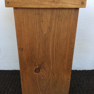May include: A wooden trash can with a hinged lid. The lid has the word "Trash" engraved on it. The can is stained a dark brown color.