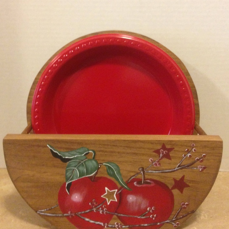 May include: A wooden plate holder with a red plate inside. The holder is painted with a design of apples and branches with stars.