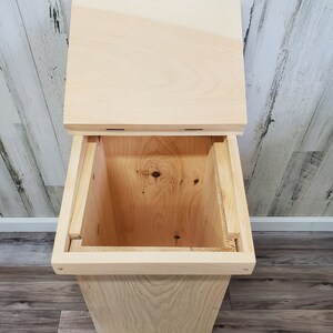 May include: A wooden bin with a hinged lid. The bin is made of natural wood and has a simple, rustic design.