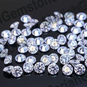 Puede incluir: Un conjunto de gemas redondas y transparentes con múltiples facetas, dispersas sobre una superficie negra. Las gemas reflejan la luz, creando un efecto brillante. Las gemas varían en tamaño y son ideales para la fabricación de joyas.