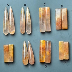 Puede incluir: Una colección de ocho pares de colgantes y cuentas de piedras preciosas pulidas. Las piedras varían en forma, incluyendo largas gotas y barras rectangulares. Los colores van del transparente al melocotón y amarillo, con vetas e inclusiones naturales.