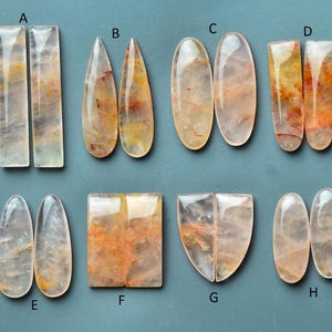 May include: Eight pairs of polished gemstones in different shapes, including rectangular, teardrop, oval, and shield. The stones are translucent, with light colours and orange and yellow inclusions.