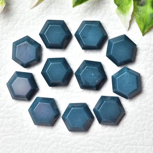 May include: A collection of eleven hexagonal, teal-colored gemstones. Each stone has a polished surface and a symmetrical shape. The gemstones are arranged in a circular pattern, suggesting they could be used for jewelry or decorative purposes.