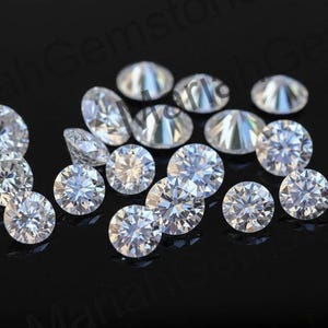 Può includere: Una collezione di diamanti rotondi e taglio brillante. Le gemme chiare e scintillanti sono sparse su una superficie nera, riflettendo la luce. I diamanti, di varie dimensioni, mettono in mostra le loro sfaccettature.