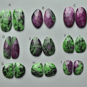 Könnte beinhalten: Neun Paare polierter Edelsteine in verschiedenen Formen. Die Steine weisen eine Mischung aus grünen und dunkelroten Farbtönen mit gesprenkeltem oder marmoriertem Aussehen auf. Die Edelsteine werden auf einer hellgrauen Oberfläche präsentiert.