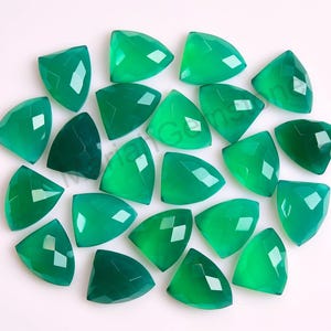 May include: A collection of loose, vibrant green gemstones, each cut into a triangular shape with multiple facets that reflect light. The stones are arranged in a cluster, displaying a consistent emerald-like hue and a polished, smooth surface finish.