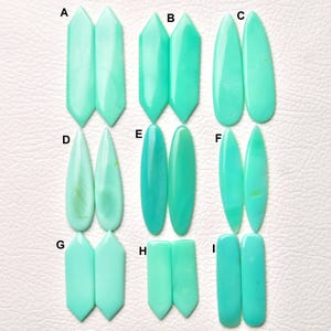 Puede incluir: Una colección de nueve pares de cabujones pulidos de color verde menta claro, etiquetados de la A a la I. Cada par presenta una forma distinta, incluyendo hexágonos alargados, gotas, óvalos y rectángulos, con una superficie lisa y opaca.