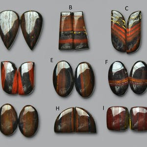 May include: Nine pairs of polished gemstones in various shapes, including teardrop, rectangular, and oval. The stones display a mix of colors, including brown, red, and black, with reflective surfaces. The gemstones are arranged on a gray background.