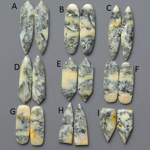 May include: A collection of nine pairs of polished gemstone cabochons, each with a unique shape and pattern. The stones feature a mix of white, gray, and yellow hues, with intricate veining and marbling. The shapes vary from pointed ovals to rectangular forms.