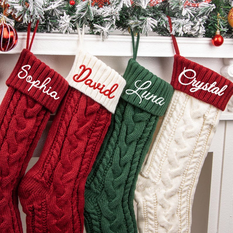 May include: Four cable-knit Christmas stockings featuring folded cuffs. The first is red with white embroidery reading Sophia, the second is red with white cuffs and red embroidery reading David, the third is green with white embroidery reading Luna, and the fourth is white with red cuffs and white embroidery reading Crystal.