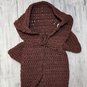 Puede incluir: Un cárdigan de punto de ganchillo marrón con capucha y cierre de nudo.