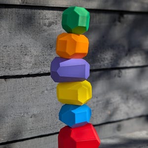 Puede incluir: Una pila de seis formas geométricas de colores, comenzando con una forma verde en la parte superior y terminando con una forma roja en la parte inferior. Las formas están apiladas sobre una superficie de madera.